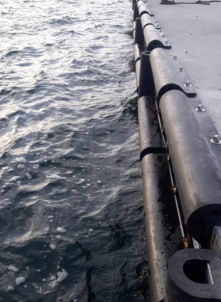 Close-up of D-section marine rubber fender mounted on a dock structure showing bolt alignment and clamping hardware.