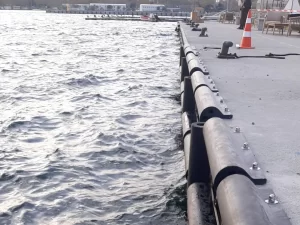 Horizontal D-type rubber fenders installed along a concrete quay wall using heavy-duty anchor bolts and clamping plates.