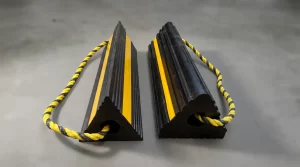 A pair of heavy-duty black rubber airplane chocks with yellow high-visibility strips and connecting rope on a pure white background.
